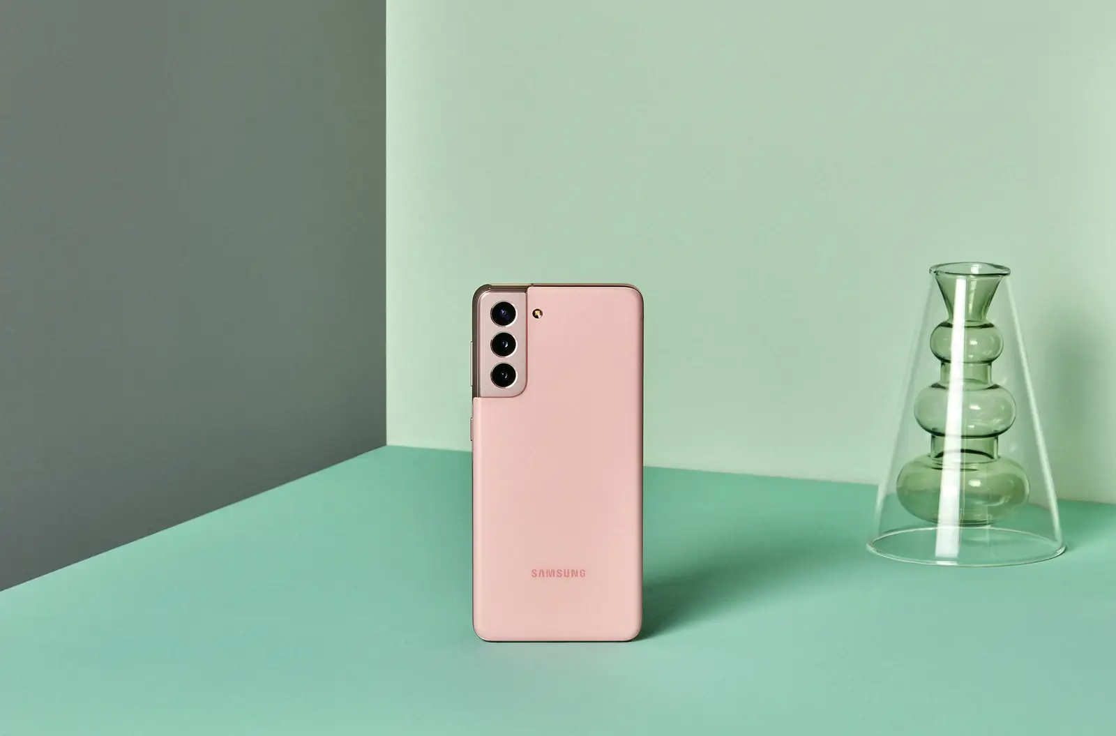 Galaxy S21 in Phantom Pink standing on a mint table beside a glass vase