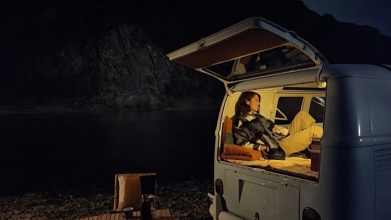 With Night mode: the van's open back, a woman reading inside, the shore and hills behind visible