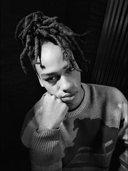 A black-and-white night portrait of a young man resting his chin on his fist