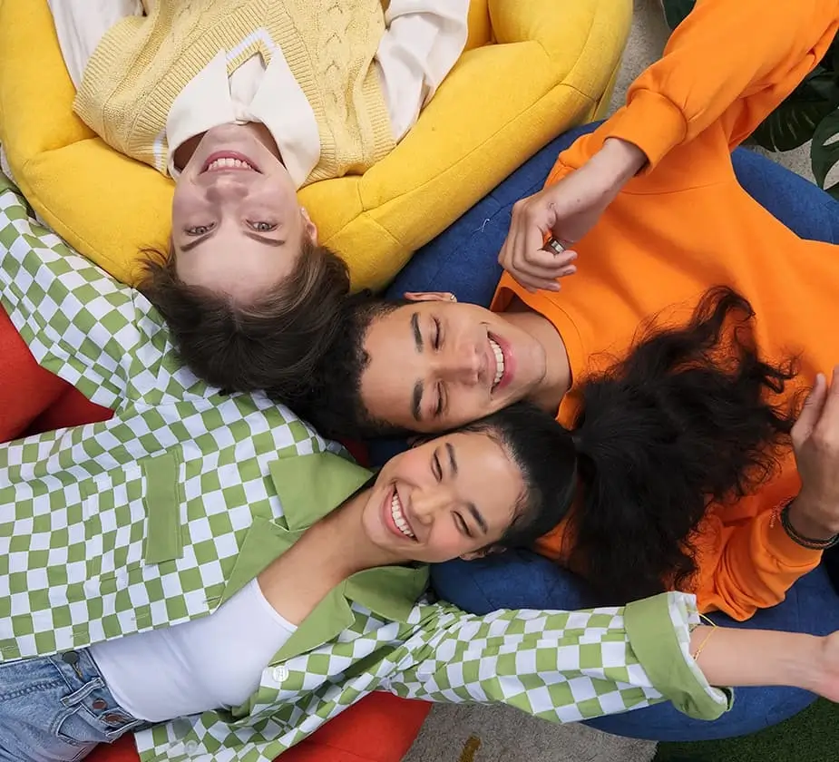 Four friends lie head to head on a rug, laughing, in bright patterned clothes