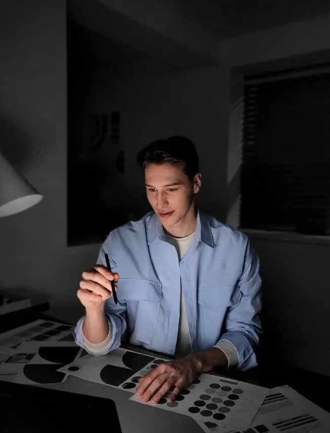 A man sketches with an S Pen at a desk in a dark room, his face clearly lit