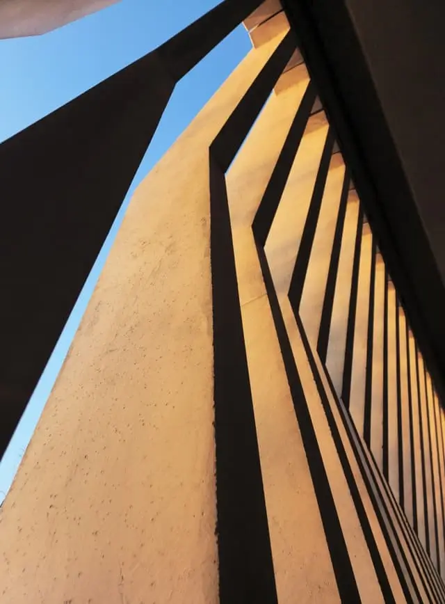 Looking up a tall ochre building with deep vertical fins against a blue sky