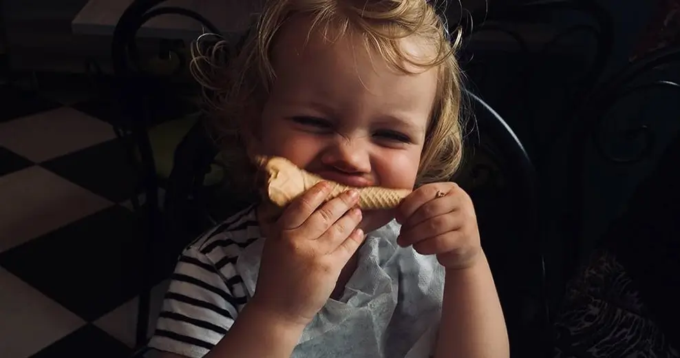 A dim, soft photo of a toddler laughing and eating a pastry