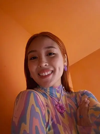 A woman takes a selfie in a dim orange room, her face evenly lit
