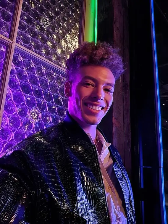A smiling man takes a selfie in a dark venue lit purple and blue