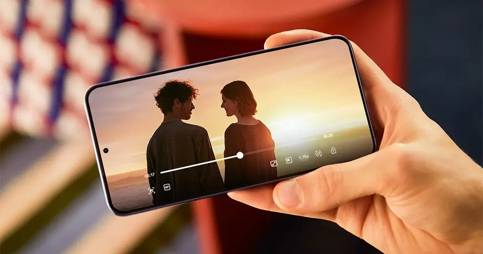 A hand holding Galaxy S24+ sideways outdoors, a sunset film scene playing on its screen