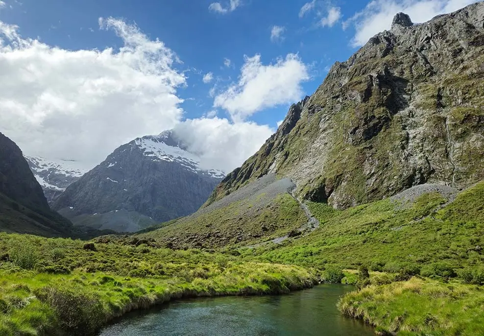 A 50MP photo of a green river valley under snow-capped mountains and a blue sky with white clouds