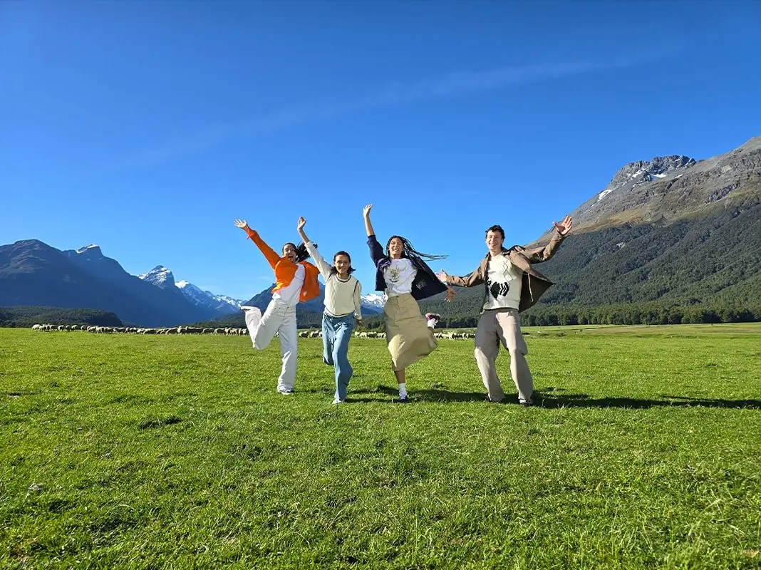 At 1x: the four friends jumping with their arms up in the field