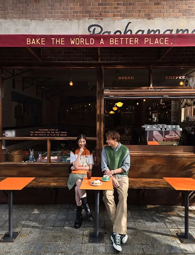 Two people at a small orange table outside a café, the whole shopfront above them