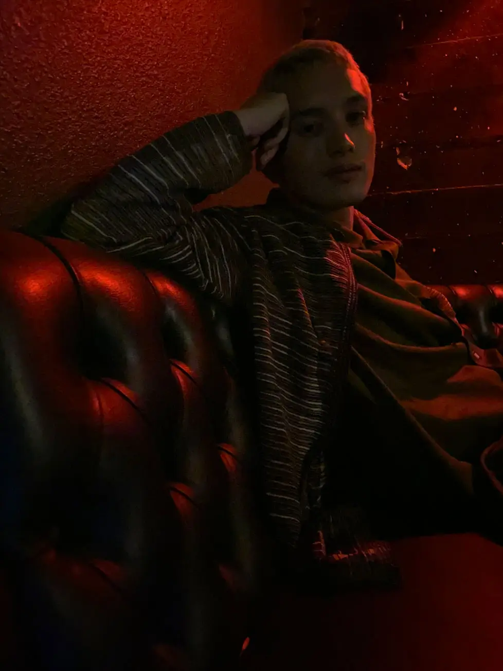 A person lounging on a leather sofa in a dark red room, photographed without Night mode: dark and murky