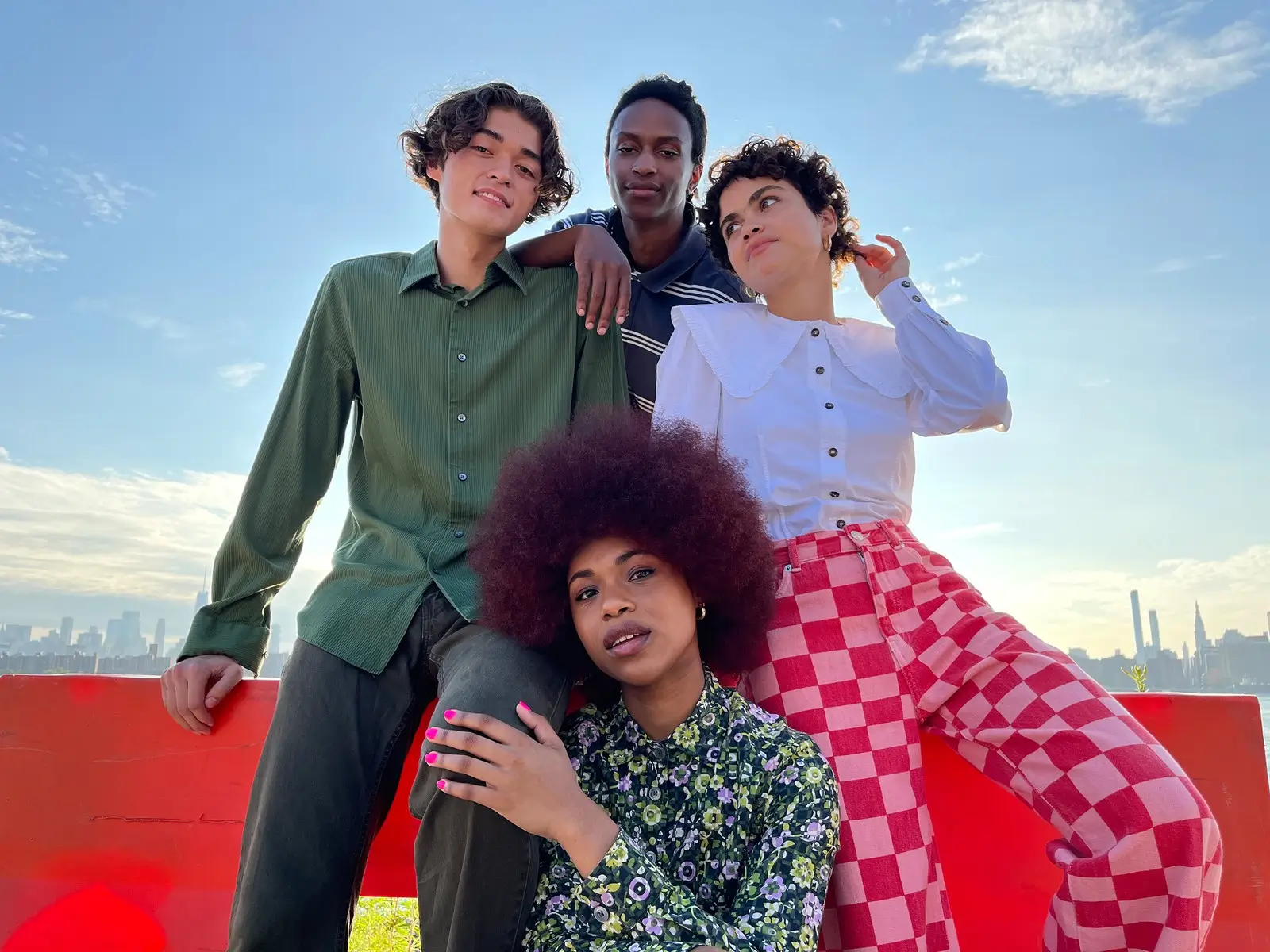 Four friends in bright clothes posing together on a rooftop under a blue sky