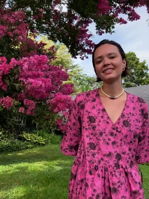 A person in a pink floral dress in front of a flowering tree, in the Standard style