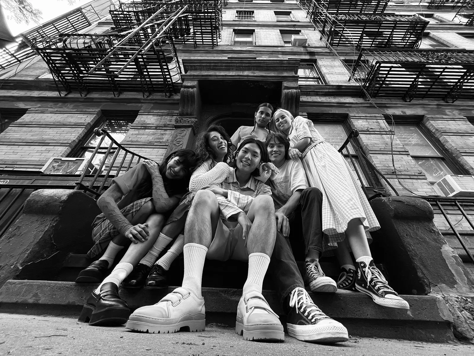 A black and white photo of a group sitting on the steps of a building with fire escapes above
