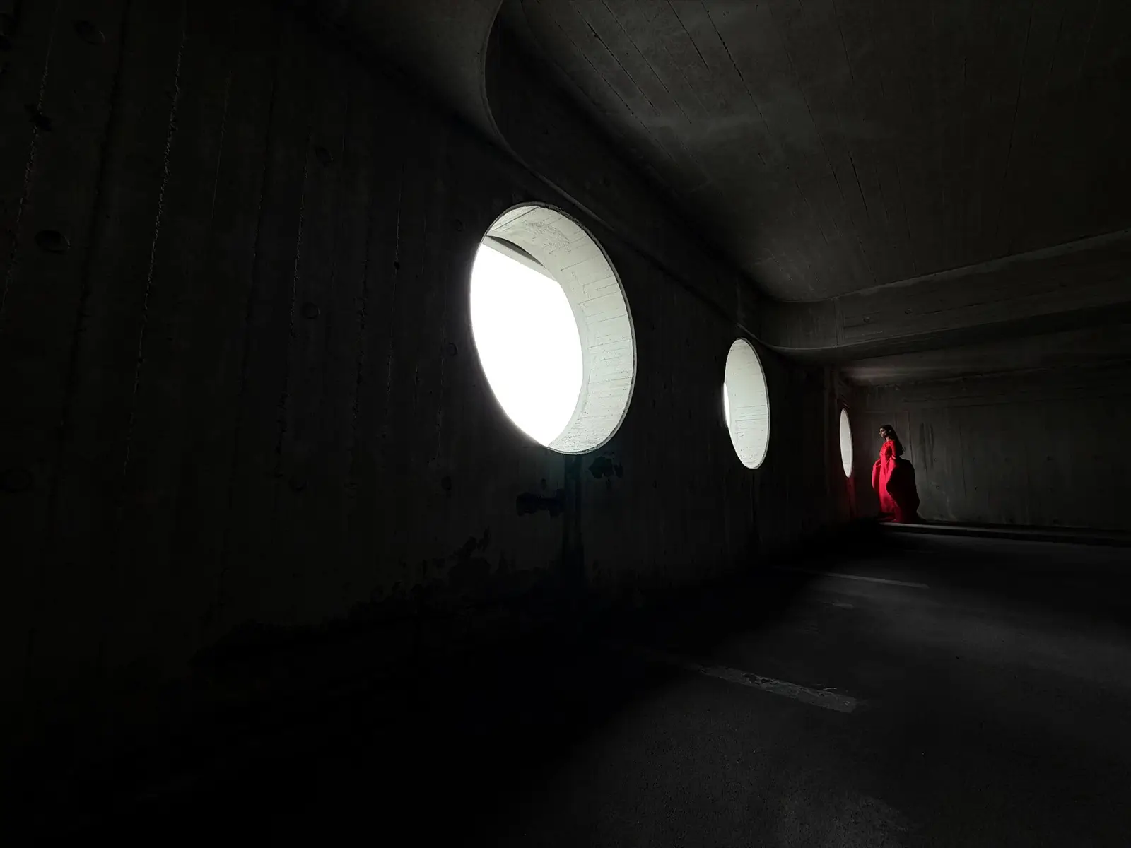 A long concrete corridor with round windows, a person in a red gown small at the far end, at 13 mm