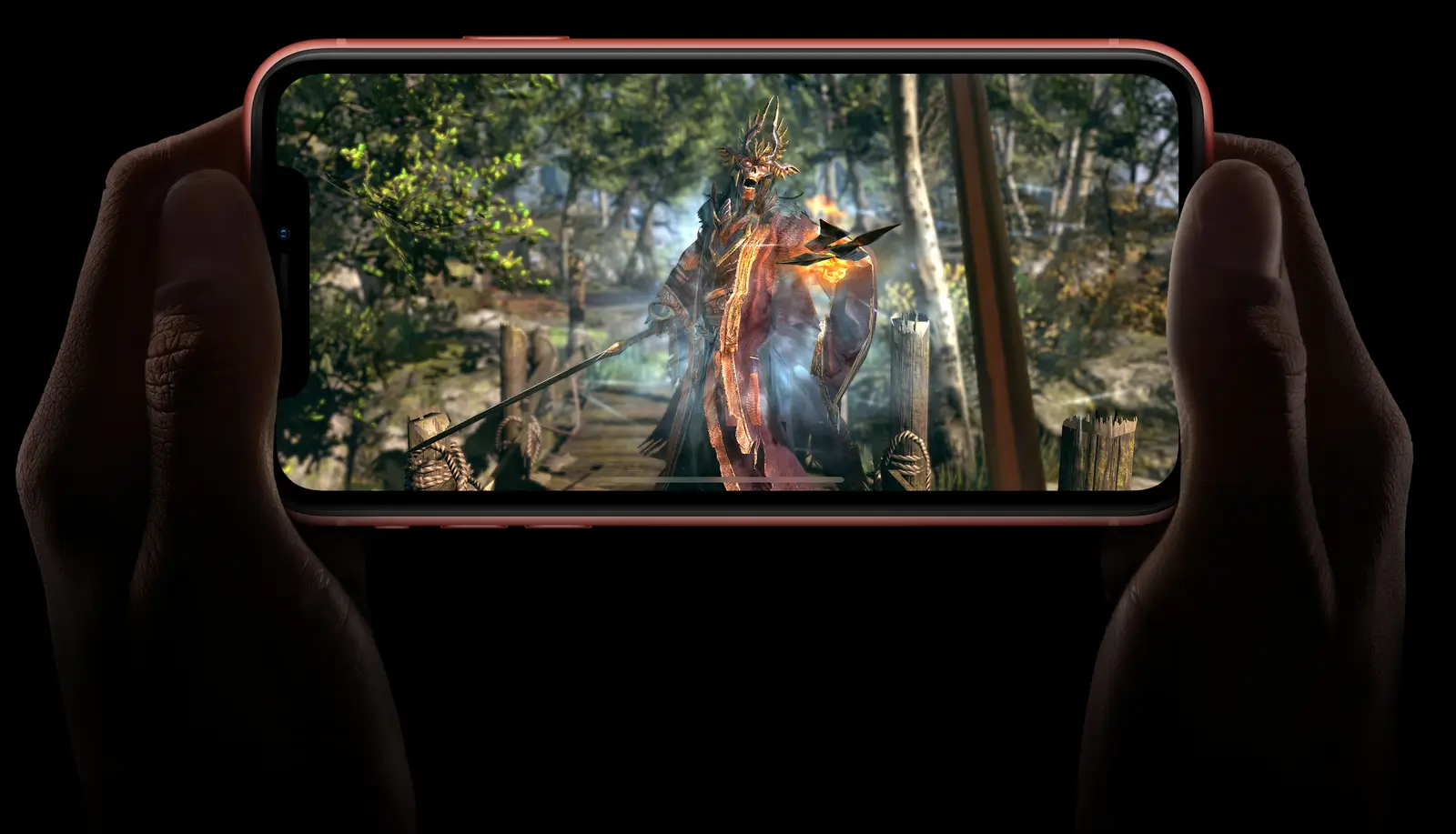 Hands holding a Coral iPhone XR sideways, playing a game in a forest