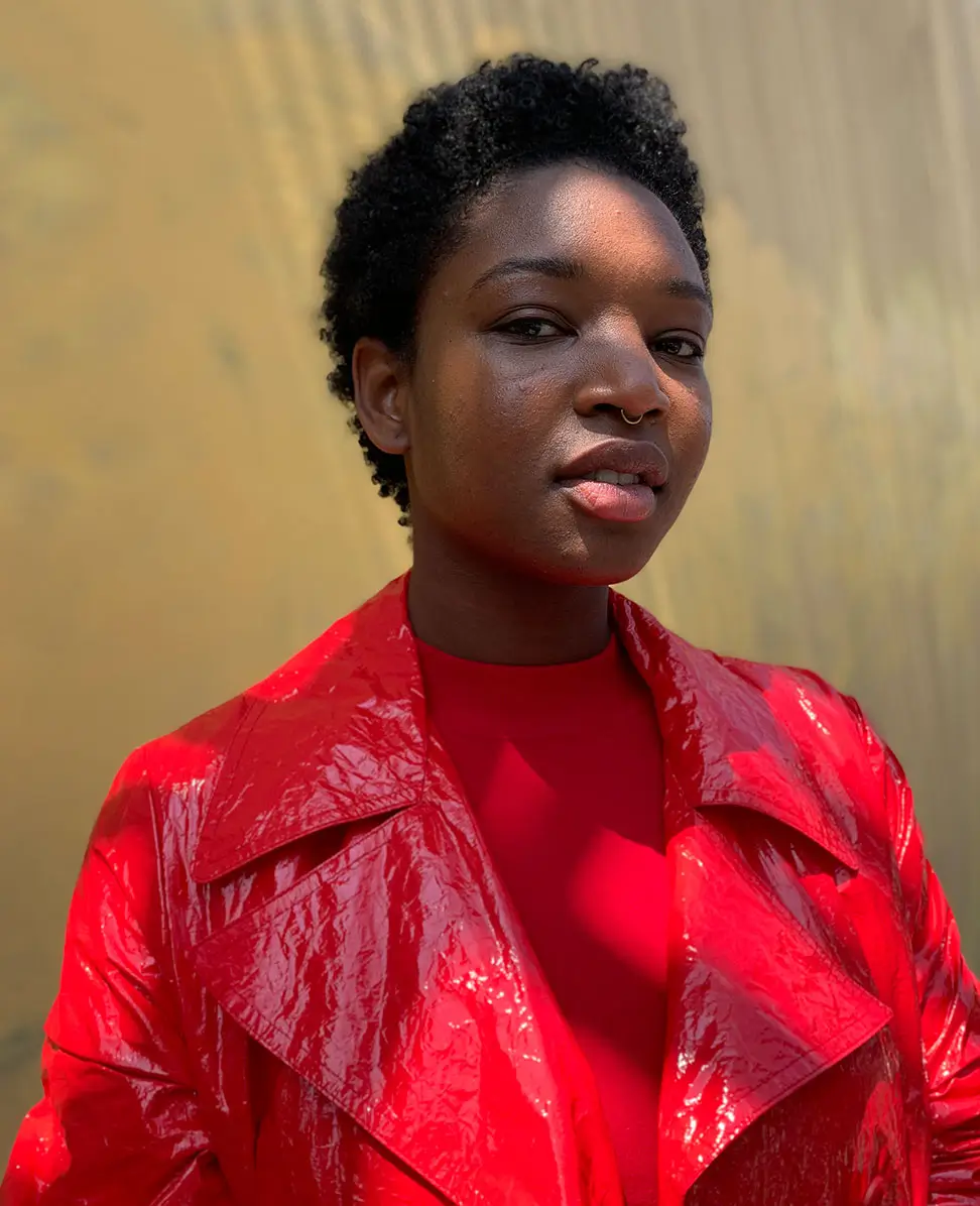 A woman in a red patent coat against a sunlit wall