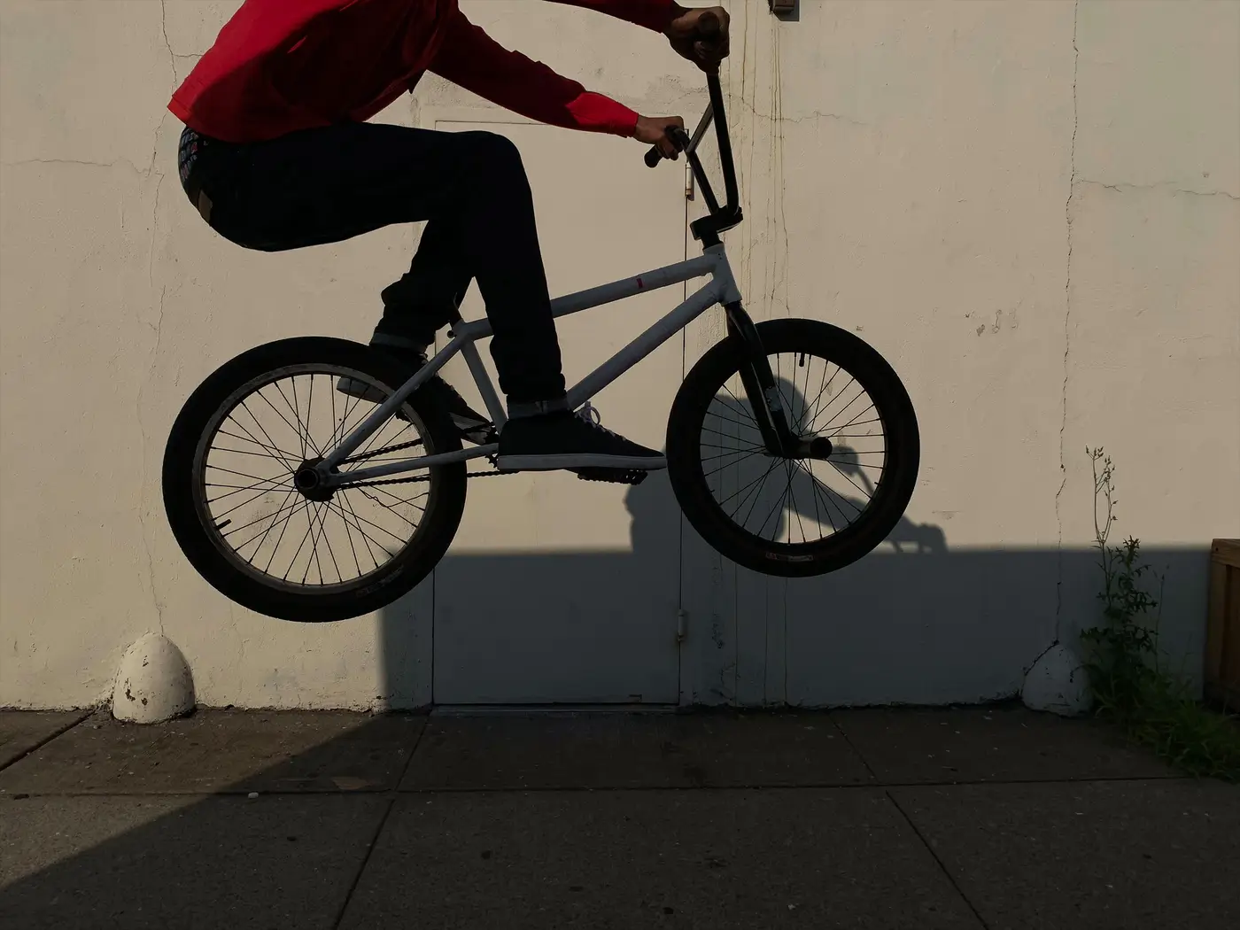 A BMX rider in the air in front of a pale wall, his shadow below