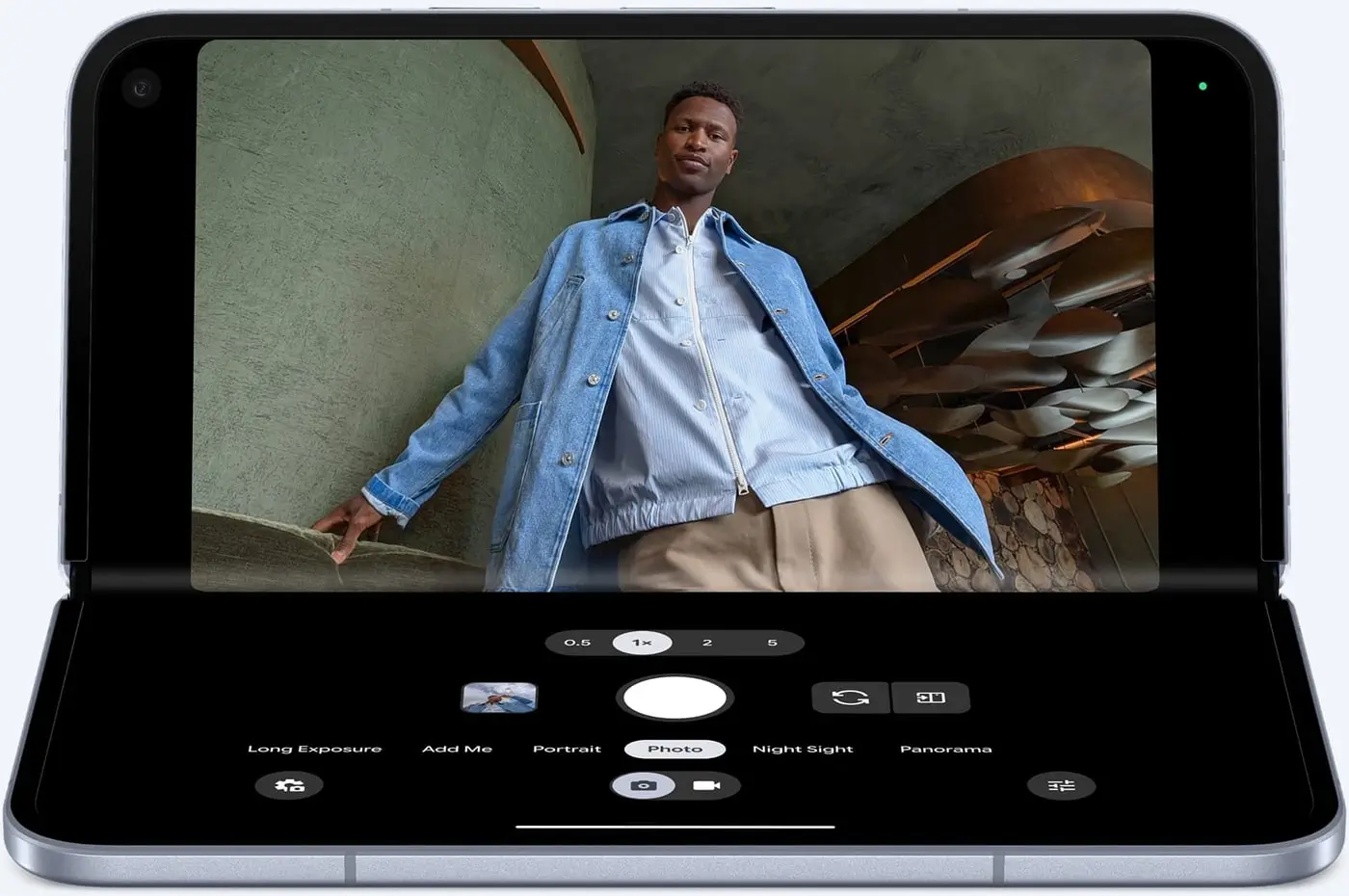 A Pixel 10 Pro Fold in tabletop mode taking a photo of a man in a denim jacket, camera controls on the lower half