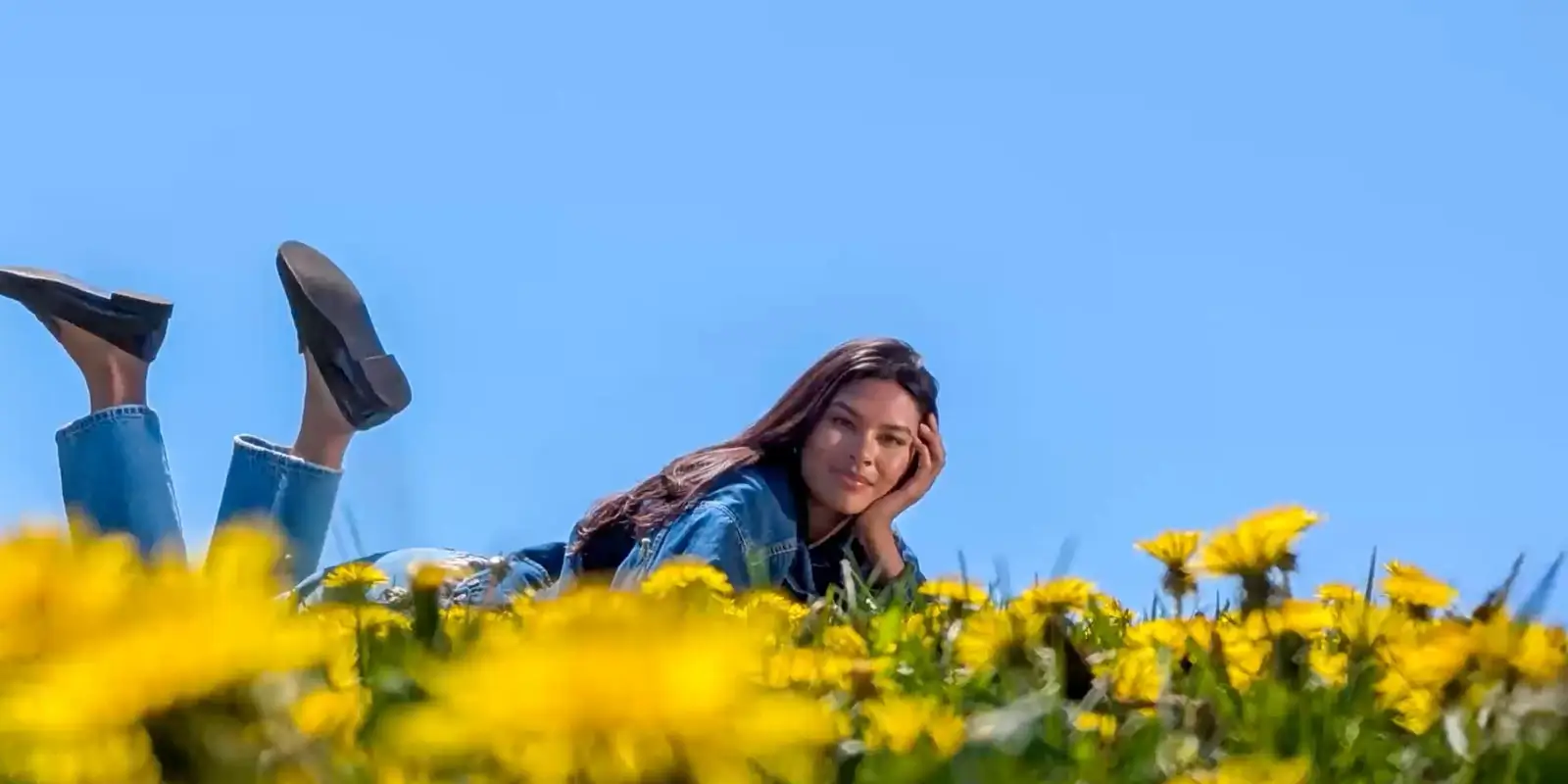 At 5x: the woman in a denim jacket lying in the flowers, chin on her hand, feet in the air