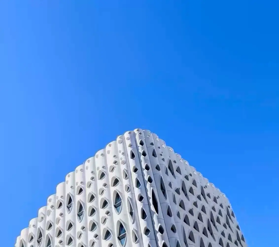 At 0.5x: the top of a white building covered in curved, eye-shaped windows against a deep blue sky