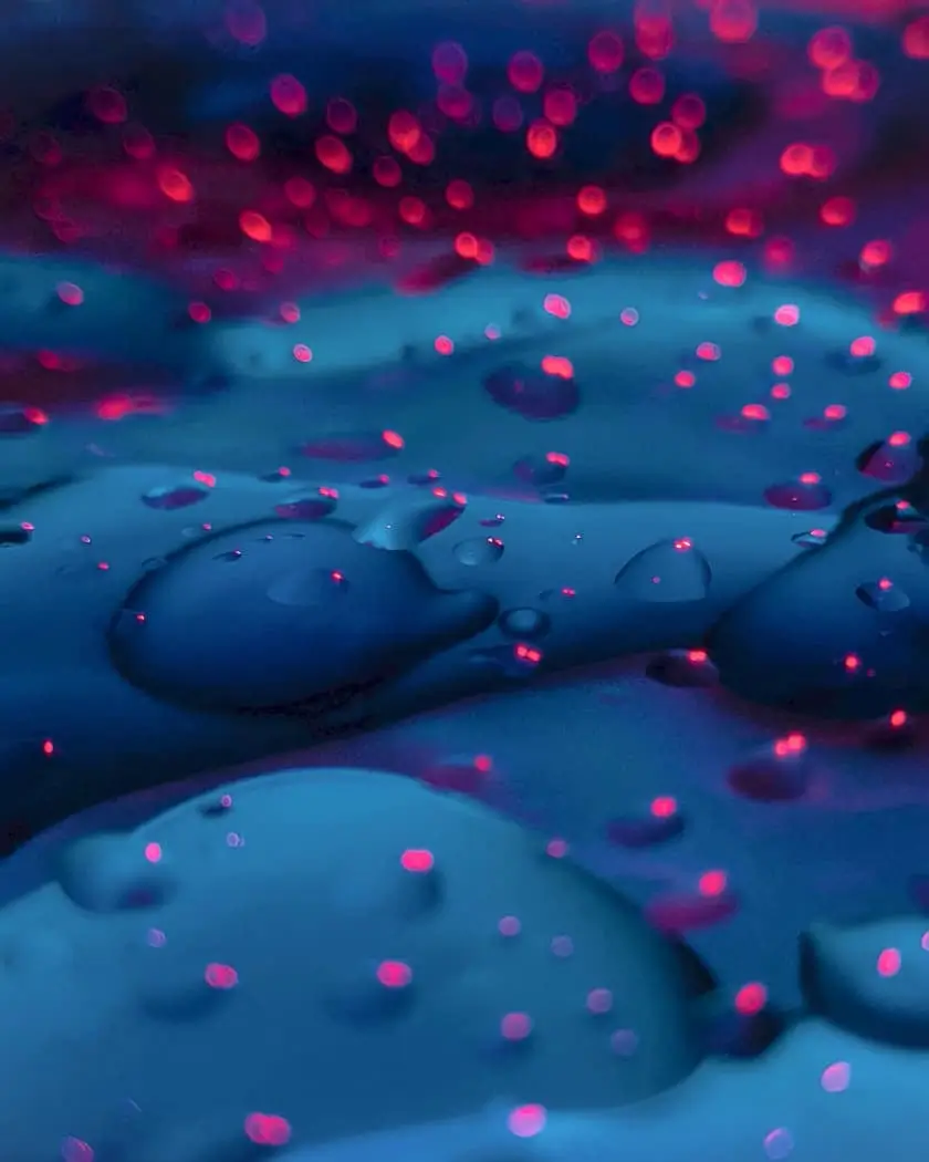 Macro Focus: freckles of red light and water droplets on a blue surface
