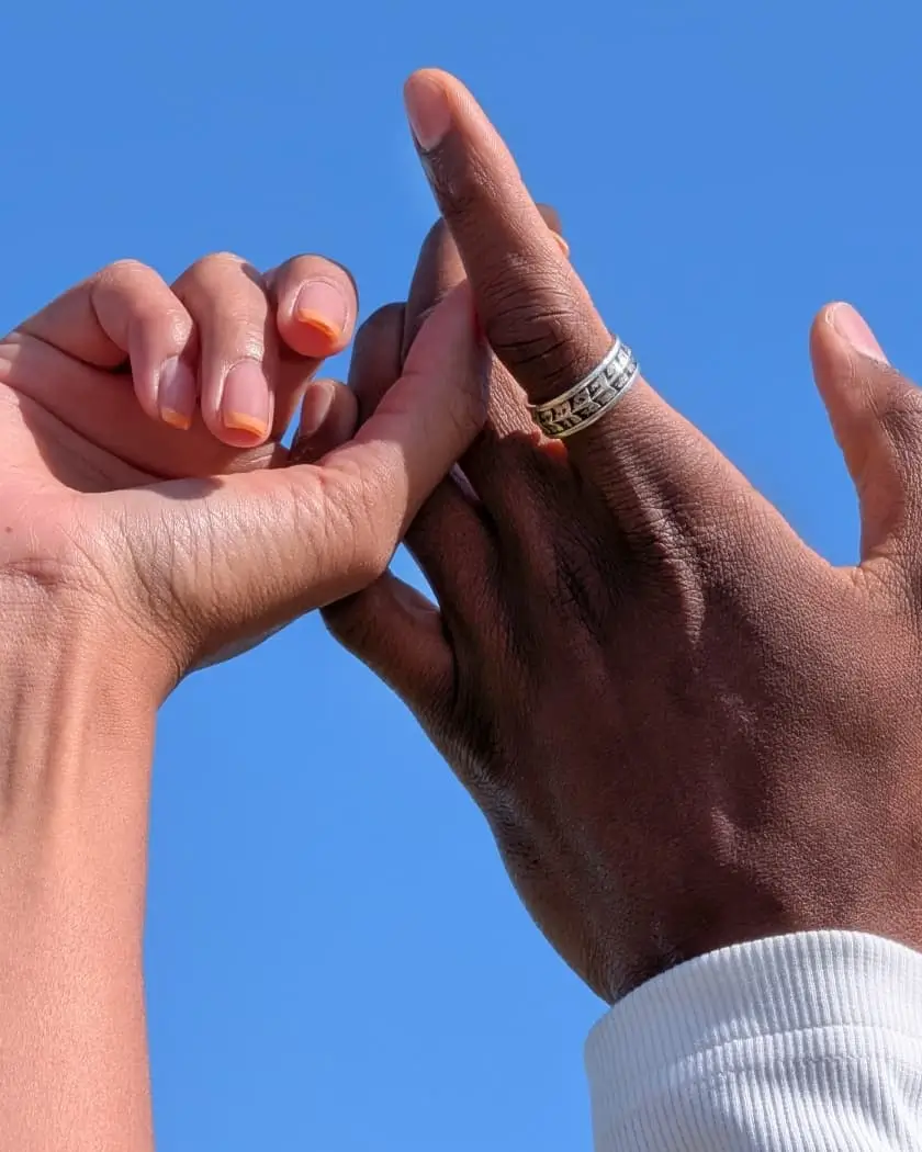 Telephoto: two hands interlace fingers, the wrinkles and a ring's etchings sharp
