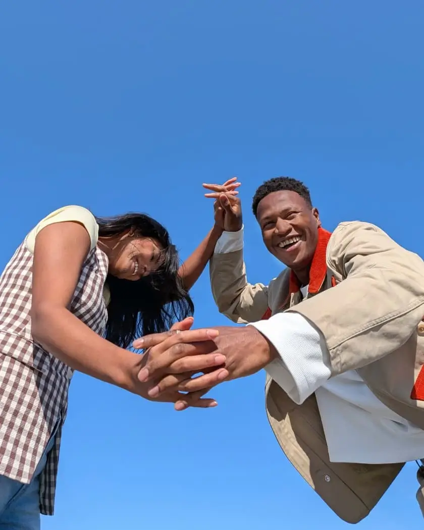 Wide: two people smile and clasp hands against a blue sky