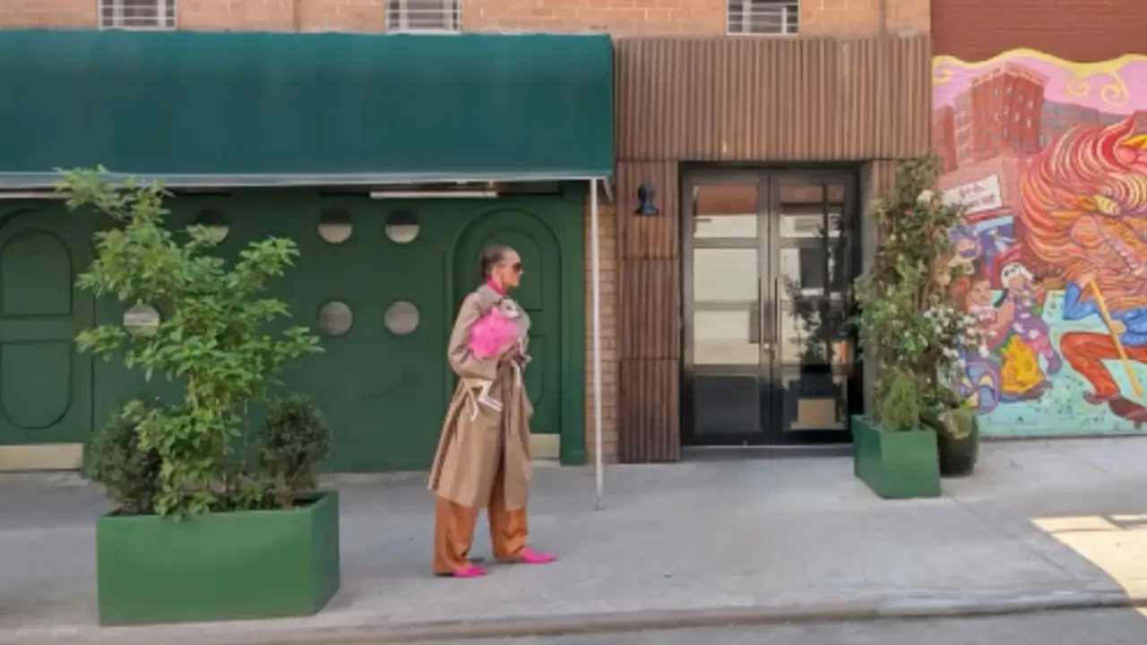 A shopfront across the street with a green awning and a mural, a woman in a trench coat small by the door