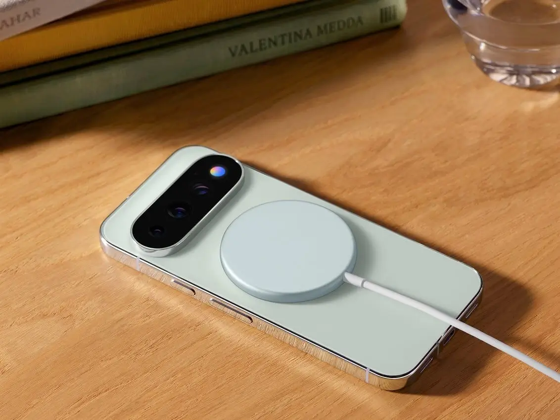 A Fog Pixel 11 Pro phone lies on a wooden desk with a Pixelsnap wireless charger attached to its back