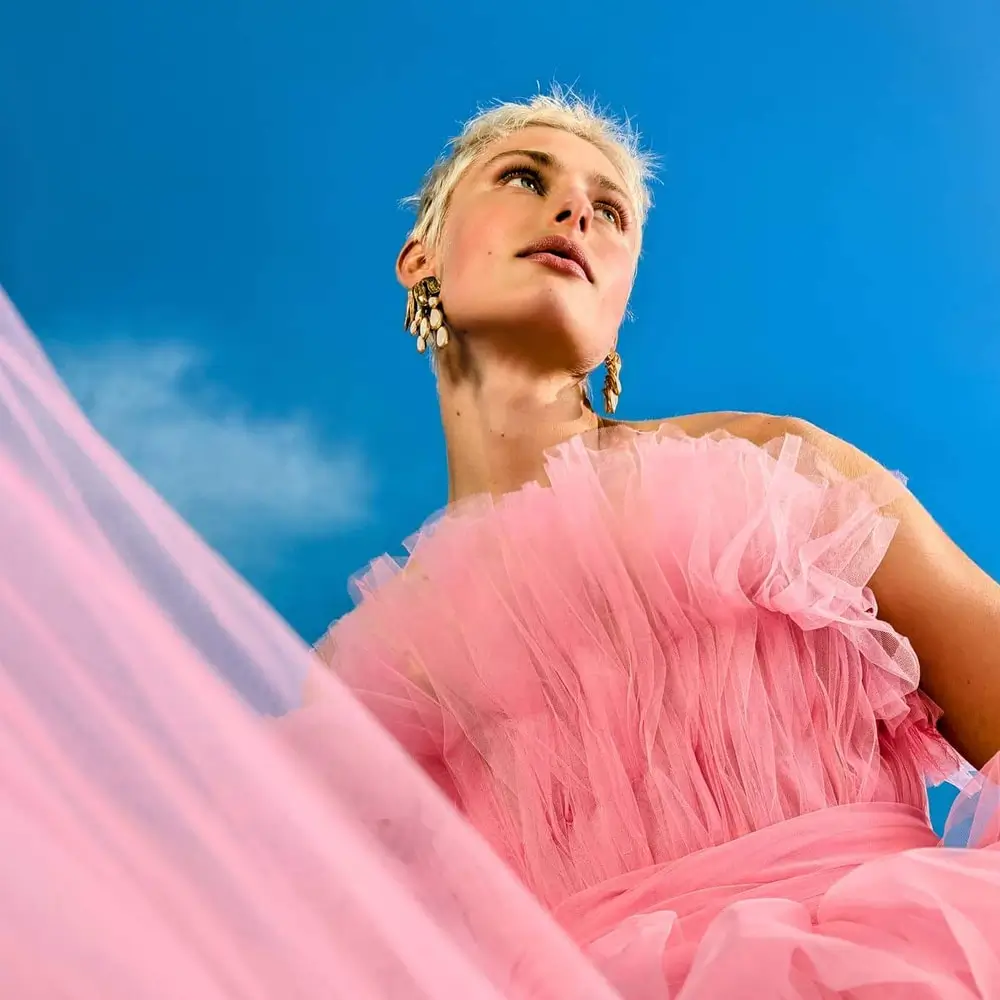 Wide: a woman in a pink tulle dress shot from below against a blue sky