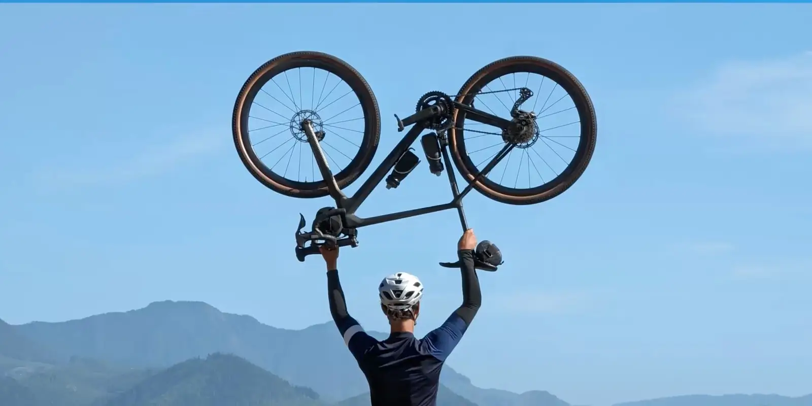 At 5x: the cyclist from the waist up, his bike held high against the sky and hills