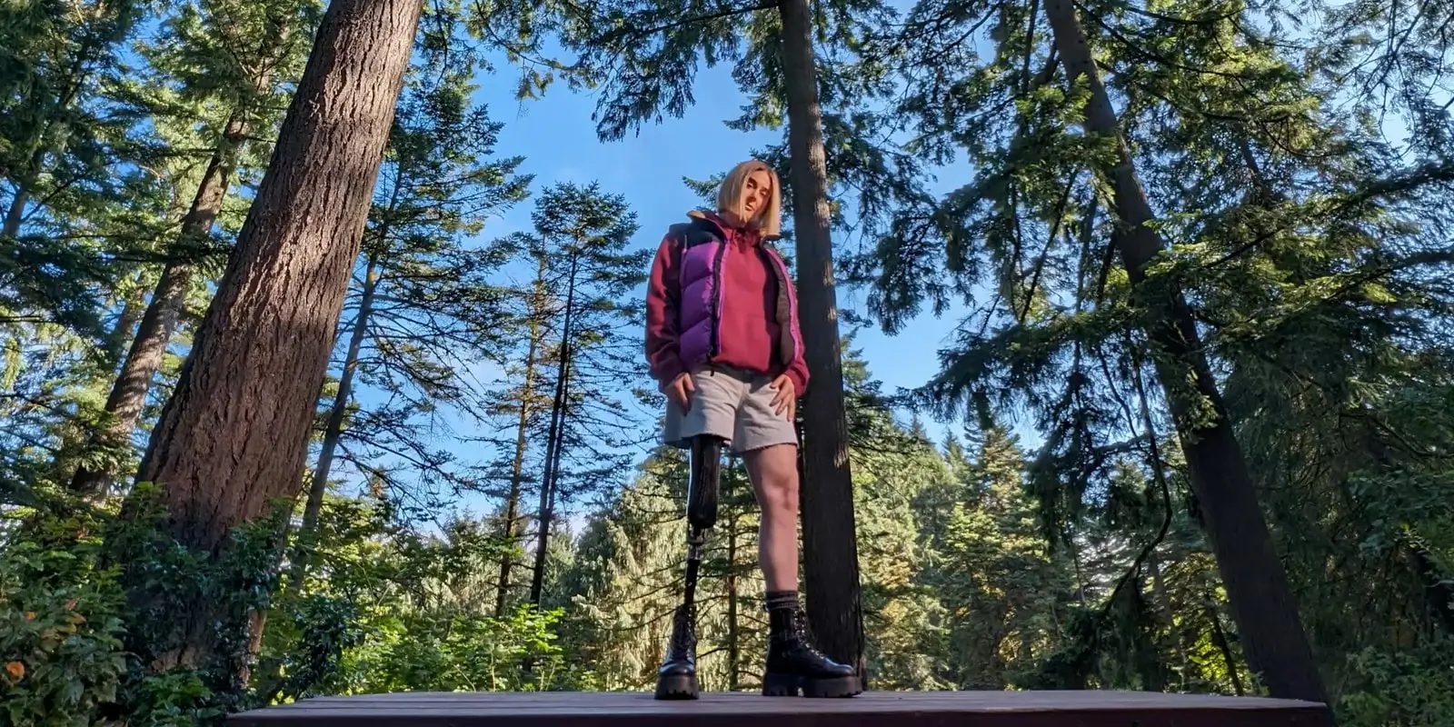 At 0.5x: tall pine trees around a woman standing on a picnic table, seen from below