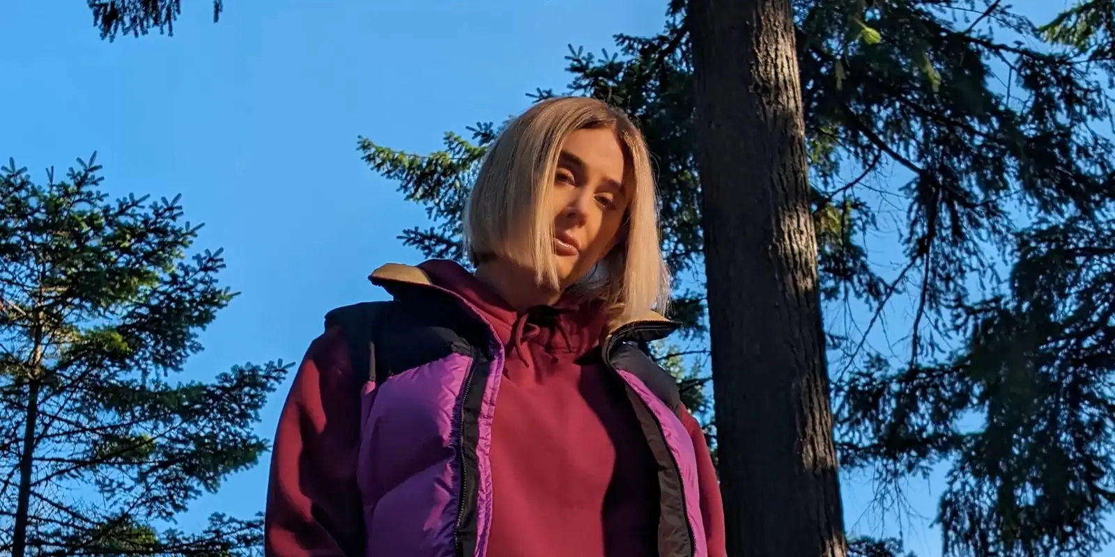 At 2x: the woman's face and jacket, a pine trunk behind her