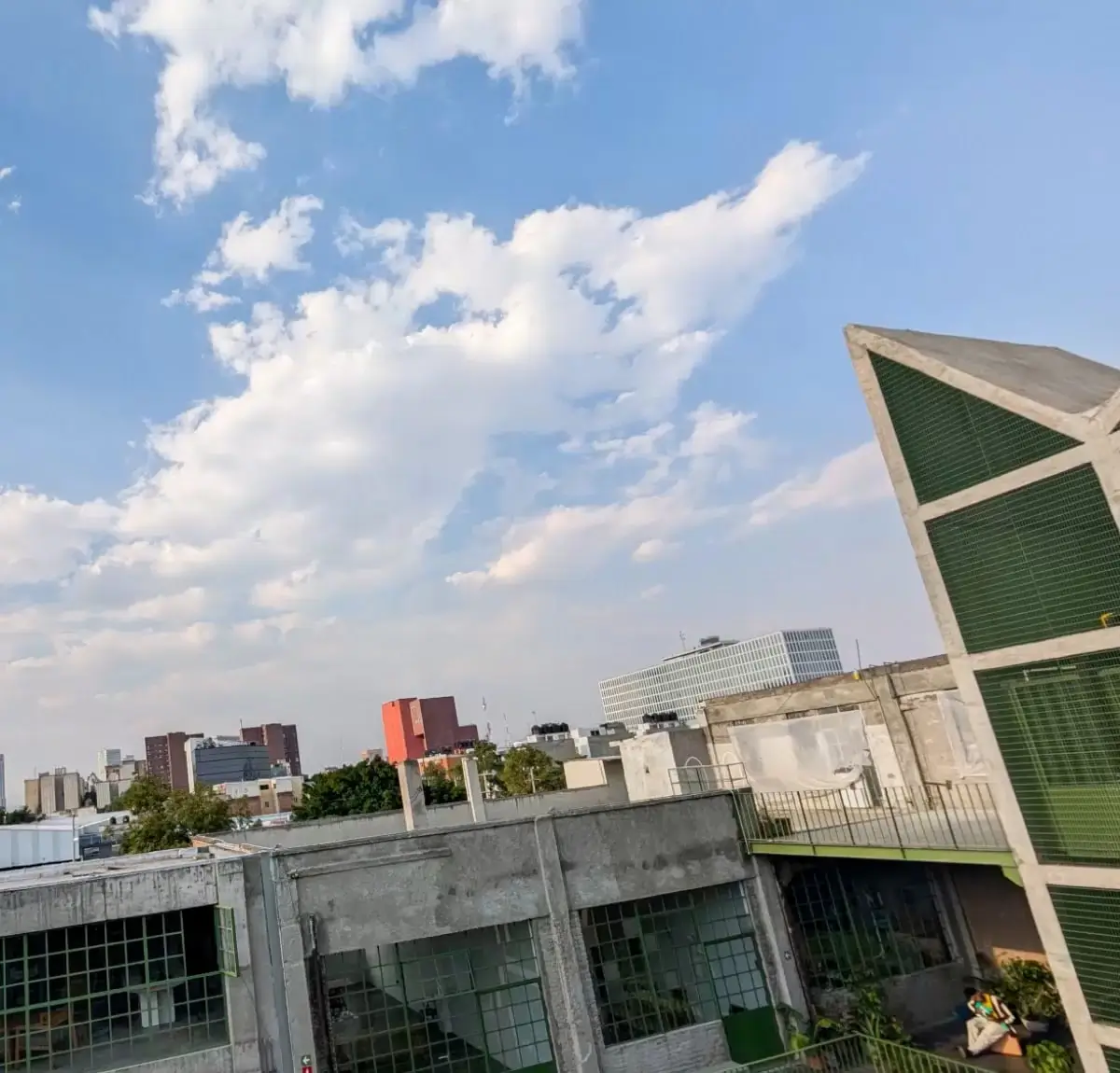 At 0.5x: a wide sky over rooftops and a city skyline, a green-framed building on the right, a man small on a balcony