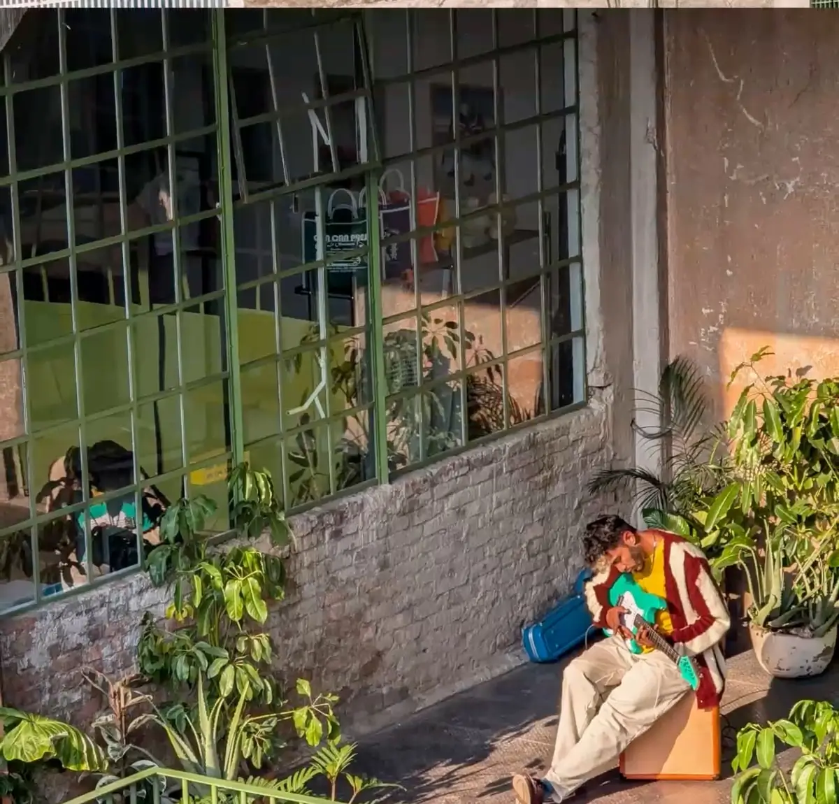 At 8x: the man on the balcony playing a turquoise electric guitar beside the plants