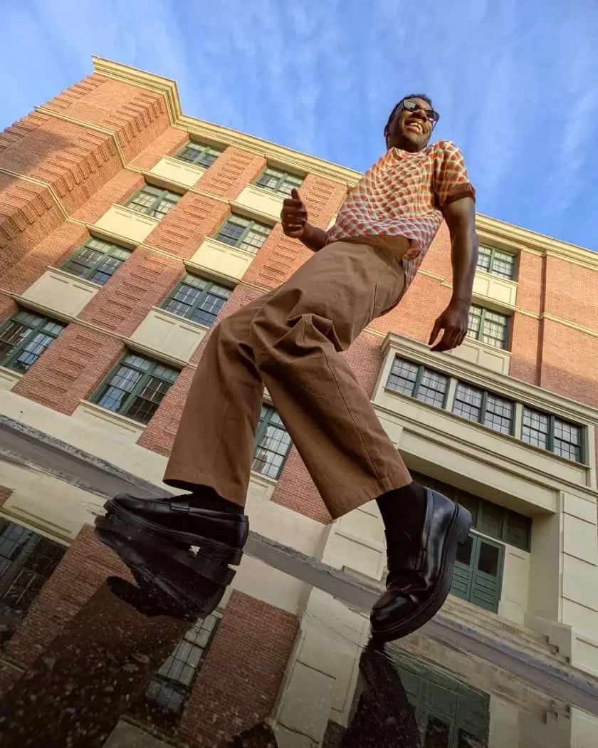 Real Tone: a man smiles as he walks past a brick building, shot from below