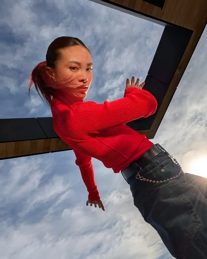 Ultra Wide: a woman in a red jumper twists against the sky, a building edge framing her